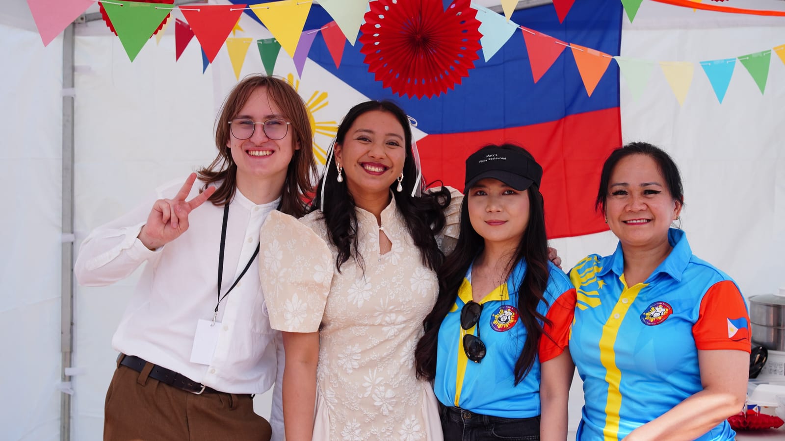 Four people in traditional Filipino dress under bunting and a Philippine flag at the Culture Festival tent
